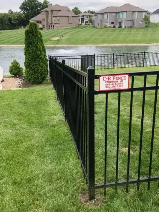 Black ornamental steel fence beside a lake with a CR Fence job sign standing at the end of the run