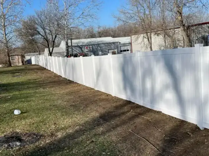 Commercial white vinyl fence job running alongside a metal shop building