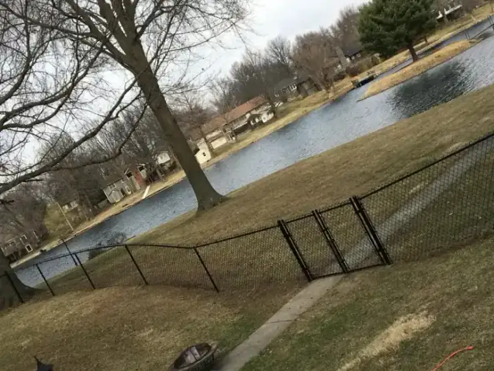 Black chain link fence and gate on a sloped lakeside yard