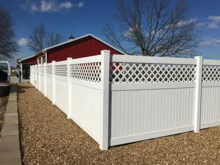 White vinyl lattice top privacy fence running past a red pole barn under open Missouri sky
